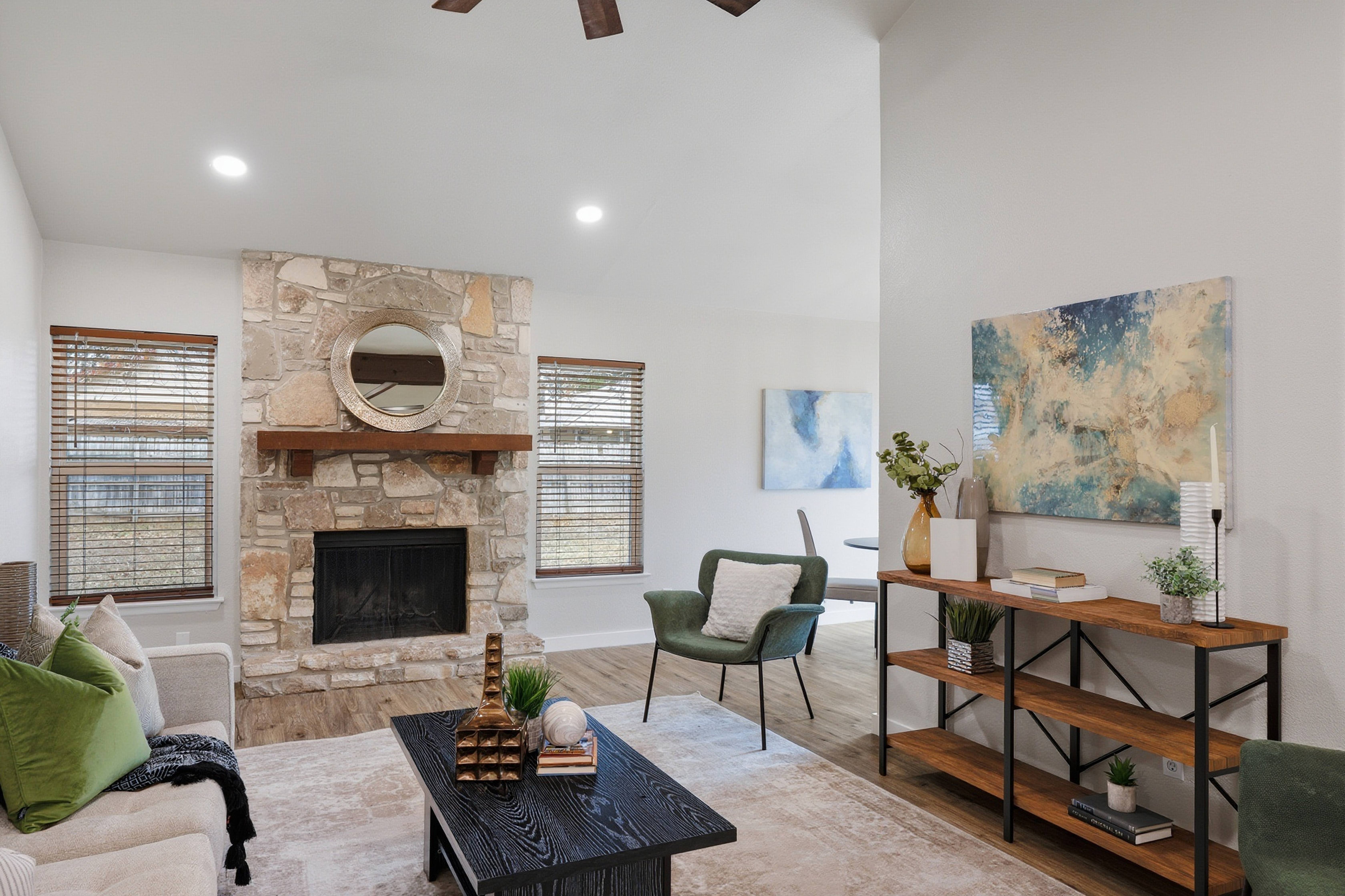 Stone fireplace focal wall in vaulted family room with green accent chairs and wood beam ceiling